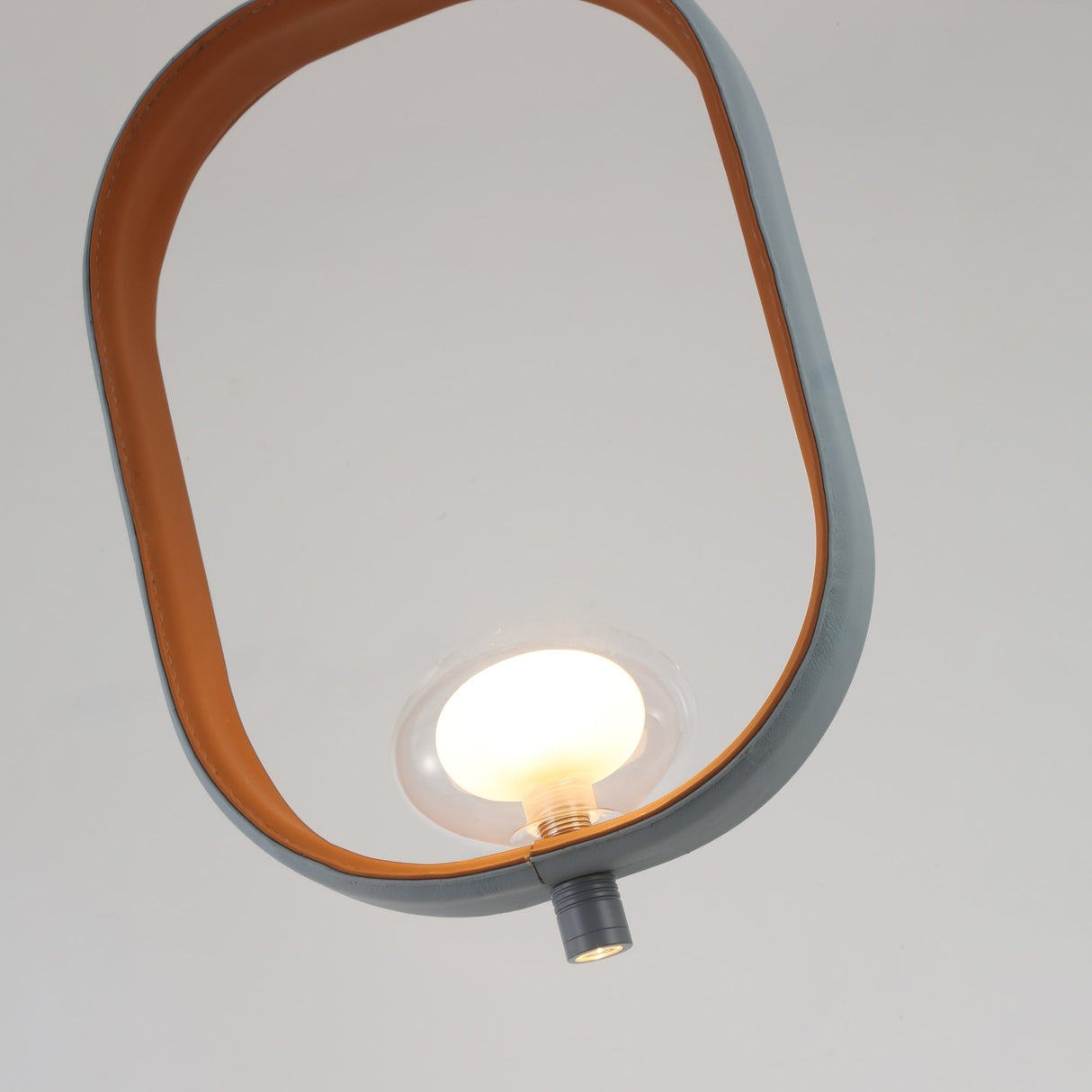 The Strappa Pendant Light - Grey/Black features a modern oval frame in gray and black with a single exposed bulb at its center, evoking the look of a lantern against a light background.