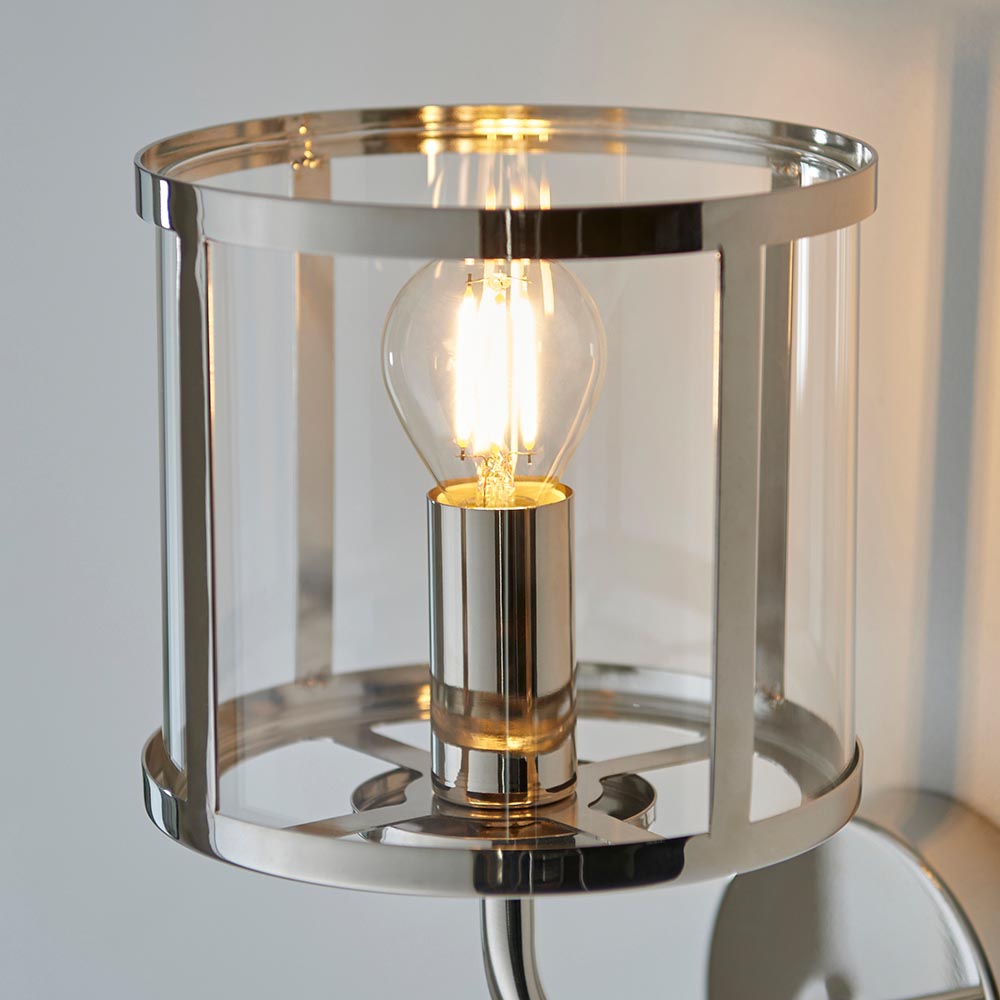 Ellery Wall Light in nickel with cylindrical clear glass shade and exposed E14 filament bulb, shown close-up against a plain light background.