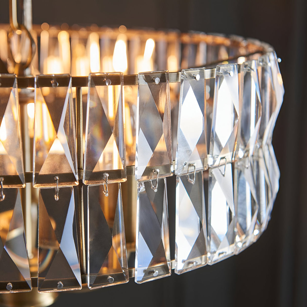 Close-up of the Endon Bevmont 3 light pendant showing tiered clear cut faceted glass panels on a brass frame with illuminated E14 lamps.