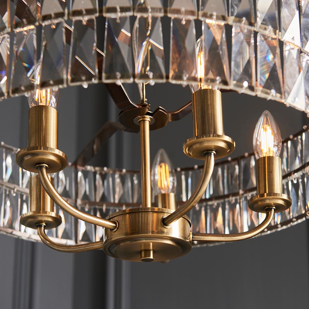 Bevmont 5 Light Pendant in antique brass, close-up of candle-style arms and E14 bulbs beneath a faceted crystal glass drum shade.