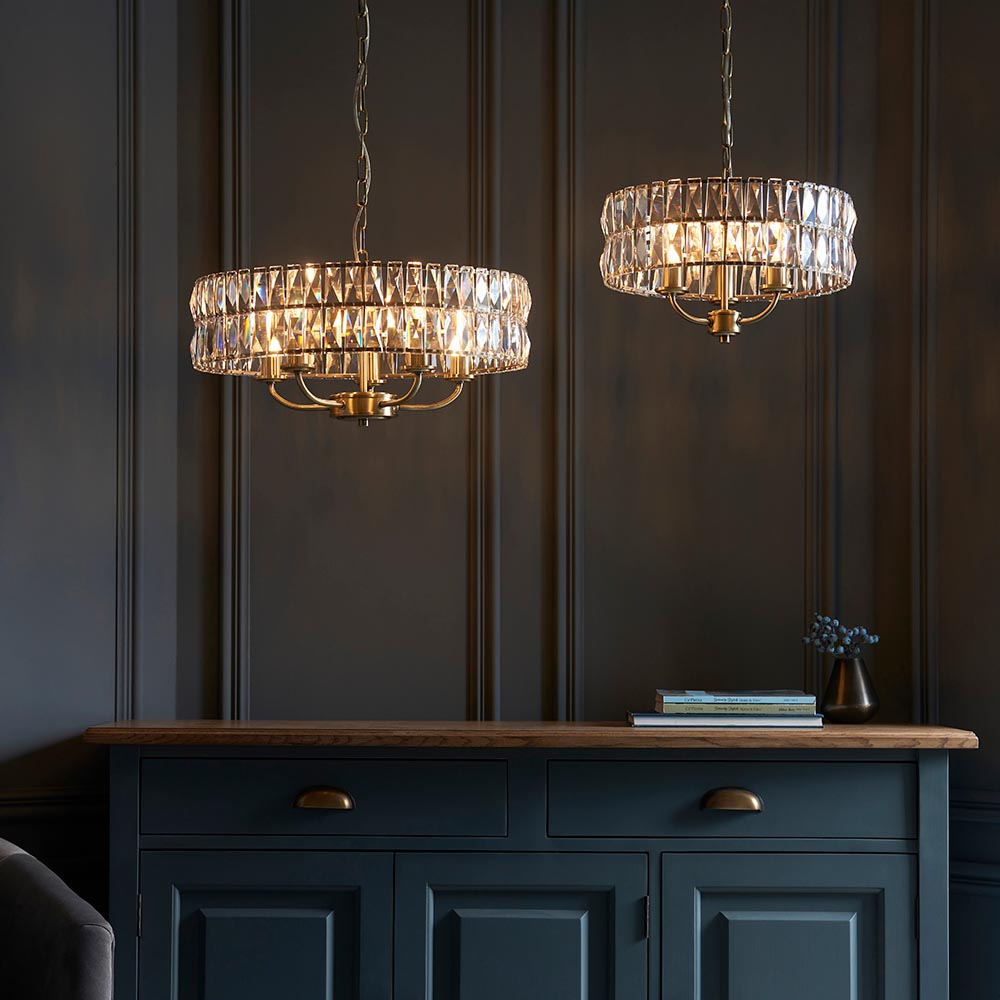 Bevmont 5 Light Pendant in brass with faceted crystal glass drum shade, shown lit above a dark blue sideboard in a panelled dining room.