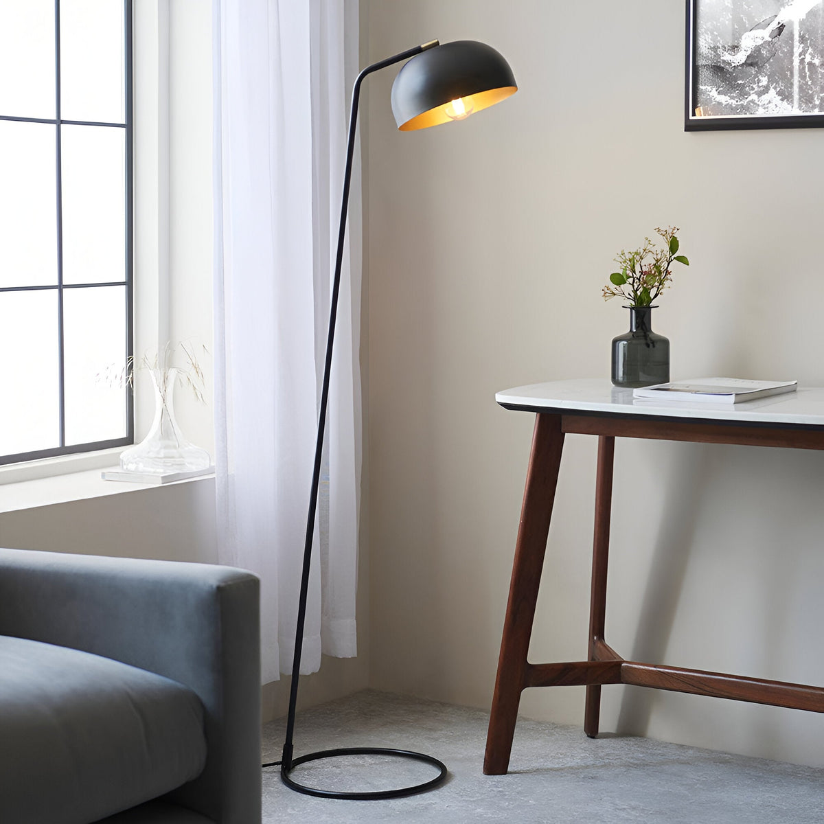 Endon Ashdon floor lamp in matt black with adjustable dome shade and brass-lined interior, beside a marble desk and grey sofa by a curtained window.