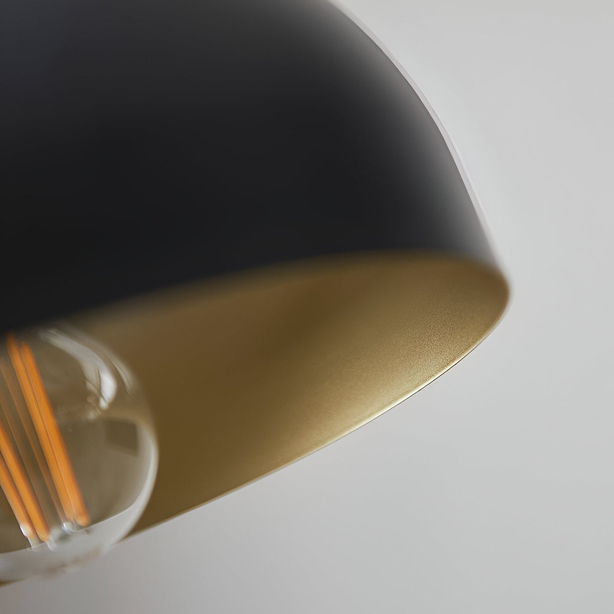 Close-up of the Endon Ashdon floor lamp's matt black dome shade with antique brass-painted interior and visible E27 filament bulb.