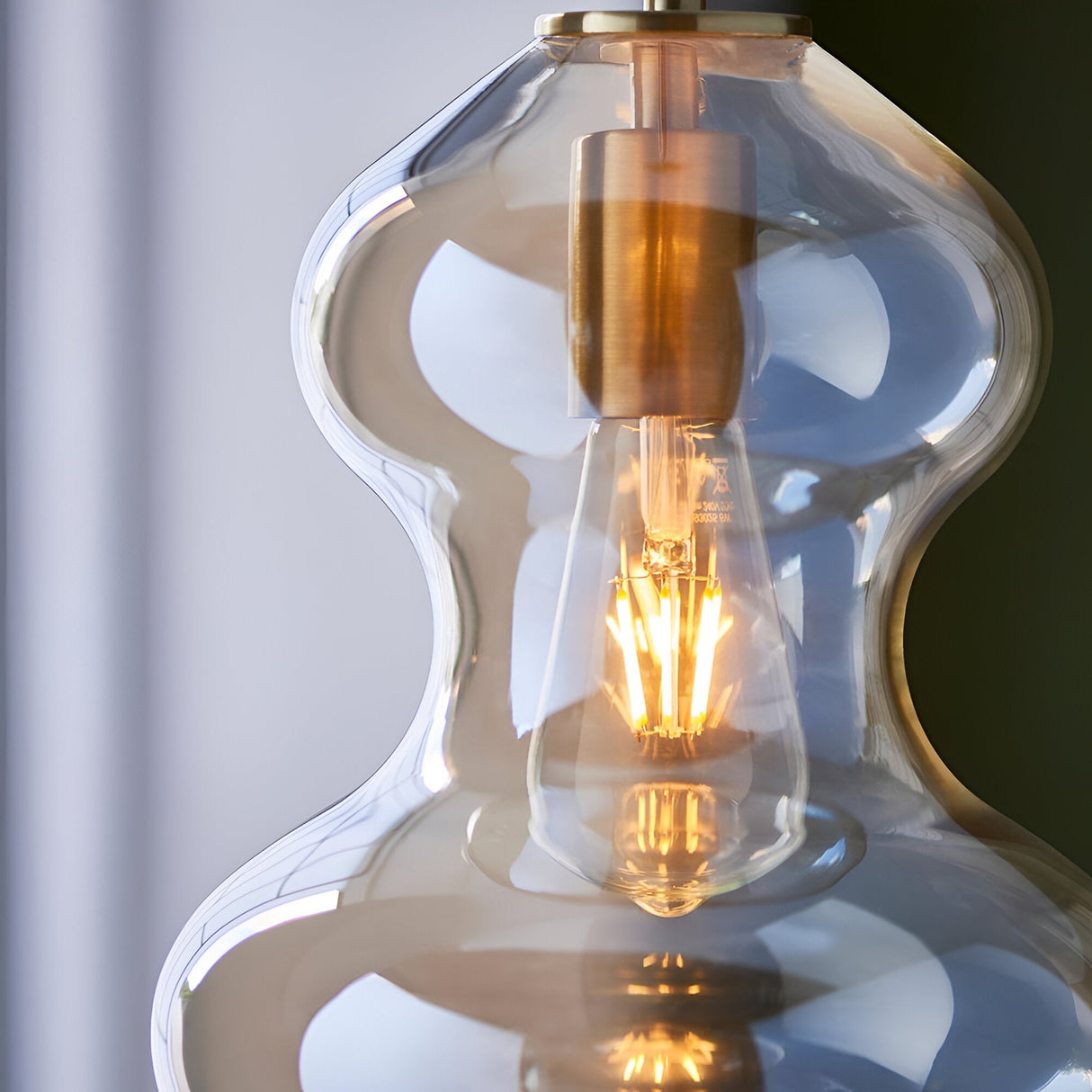 Brockley Pendant in satin brass with a curved champagne lustre glass shade, close-up showing the E27 bulb glowing inside.