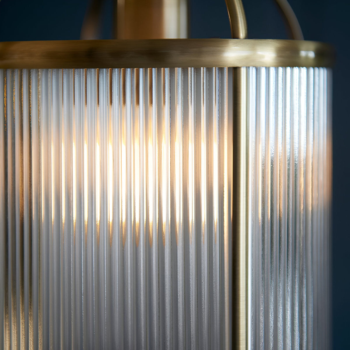 Close-up of Endon Caldcombe pendant showing clear ribbed glass panels, antique brass rim, and warm glow from the single E27 lamp within.