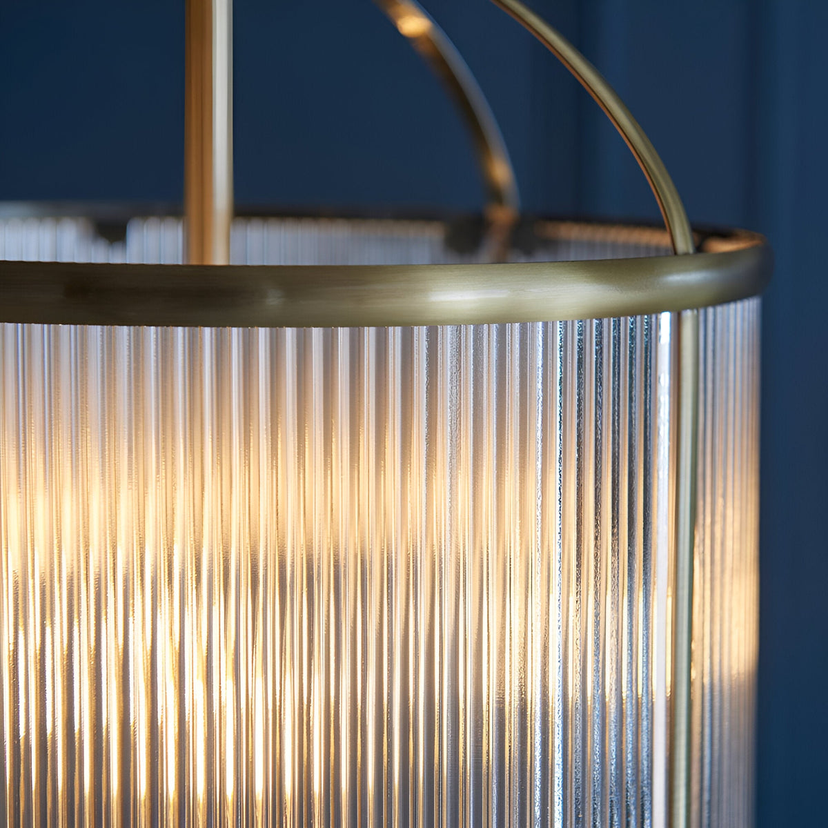 Close-up of the Endon Caldcombe pendant showing the antique brass ring and clear ribbed glass shade illuminated against a deep blue wall.