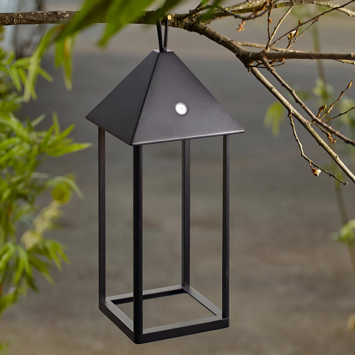 Endon Brenmont large matt black aluminium lantern table lamp with pyramid top and open frame, hanging from a tree branch outdoors.