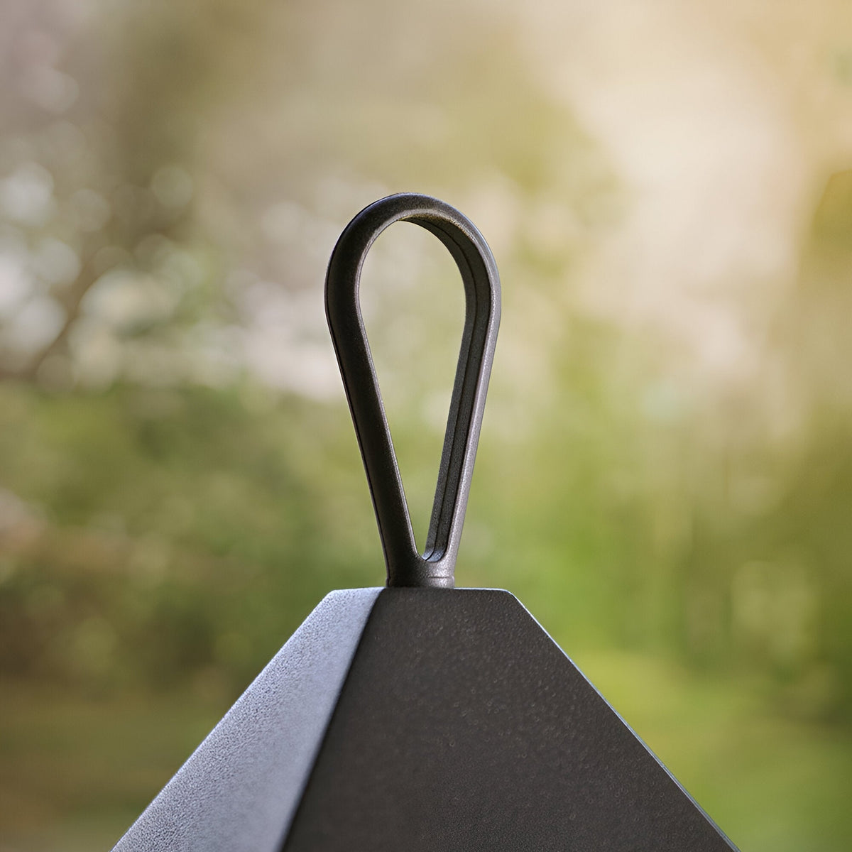 Close-up of the loop handle and matt black aluminium peaked top of the Endon Brenmont large table lantern, shown outdoors against blurred greenery.