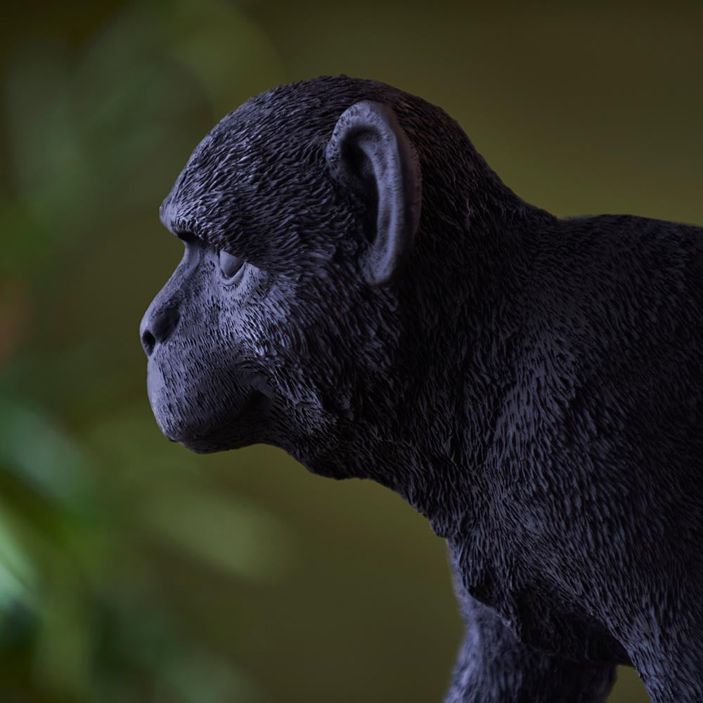Belvoir Table Lamp in black resin, close-up side profile of the detailed monkey figure base with textured fur finish, set against a blurred green backdrop.