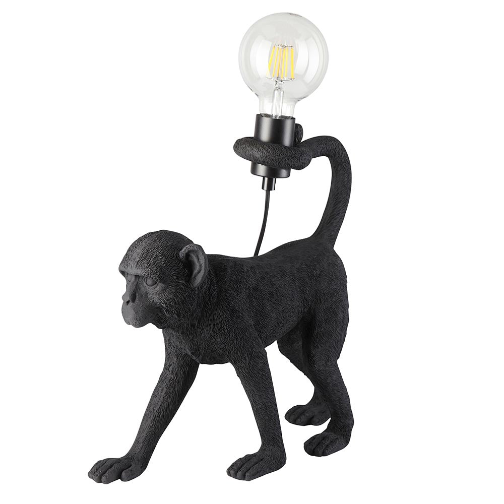 Belvoir Table Lamp in matt black resin, shaped as a walking monkey with tail raised to hold an exposed filament bulb, on a plain white background.