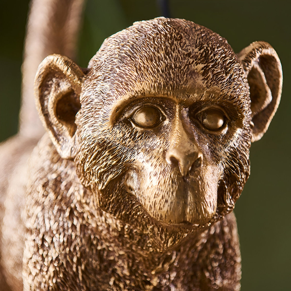 Close-up of the Endon Belvoir table lamp showing the detailed resin monkey face in a warm vintage gold finish against a soft green background.