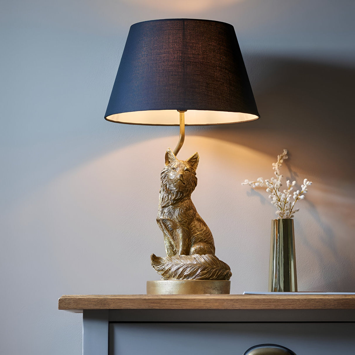 Endon Brambury table lamp with a vintage gold resin fox base and black tapered fabric shade, styled on a wooden console beside a brass vase.