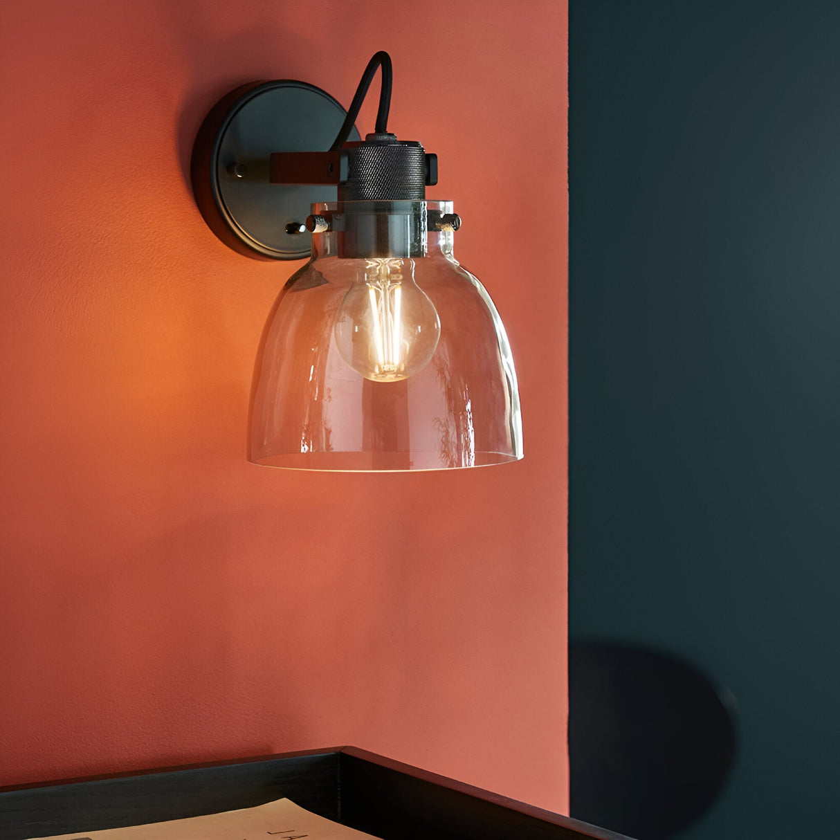 Camden Wall Light in black chrome with a clear glass dome shade and exposed bulb on a braided cable, shown mounted on a terracotta wall.