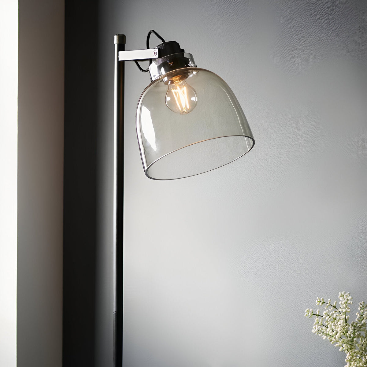 Endon Camden industrial floor lamp in matt black with adjustable head, smoked grey tinted glass shade and filament bulb, against a light grey wall.