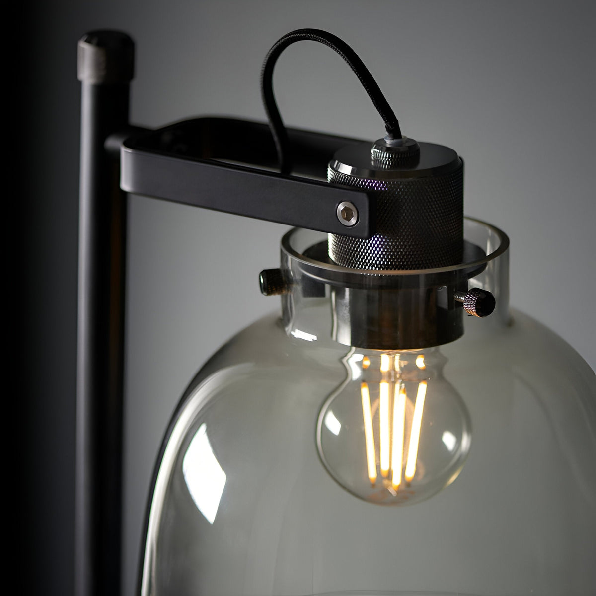 Close-up of Endon Camden Task Floor Lamp in matt black with knurled chrome details and smoked grey glass shade housing a lit E27 filament bulb.