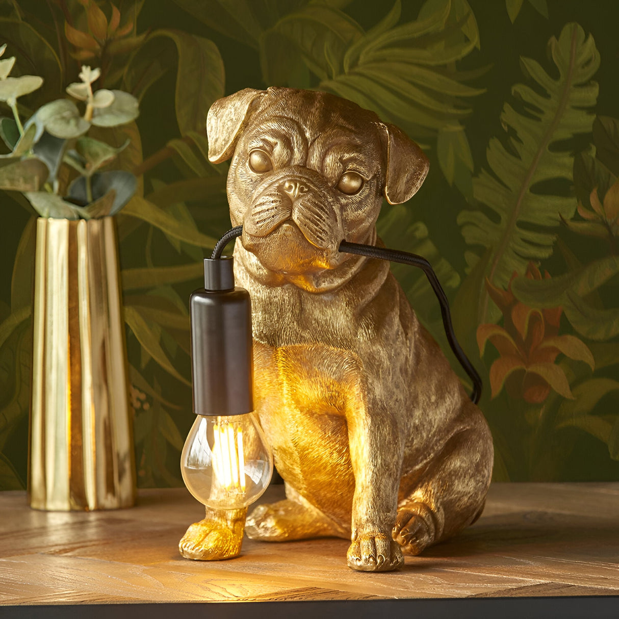 Endon Charthurst table lamp shaped as a gold resin pug figure holding a black E14 lamp holder with exposed filament bulb, on a wooden shelf.