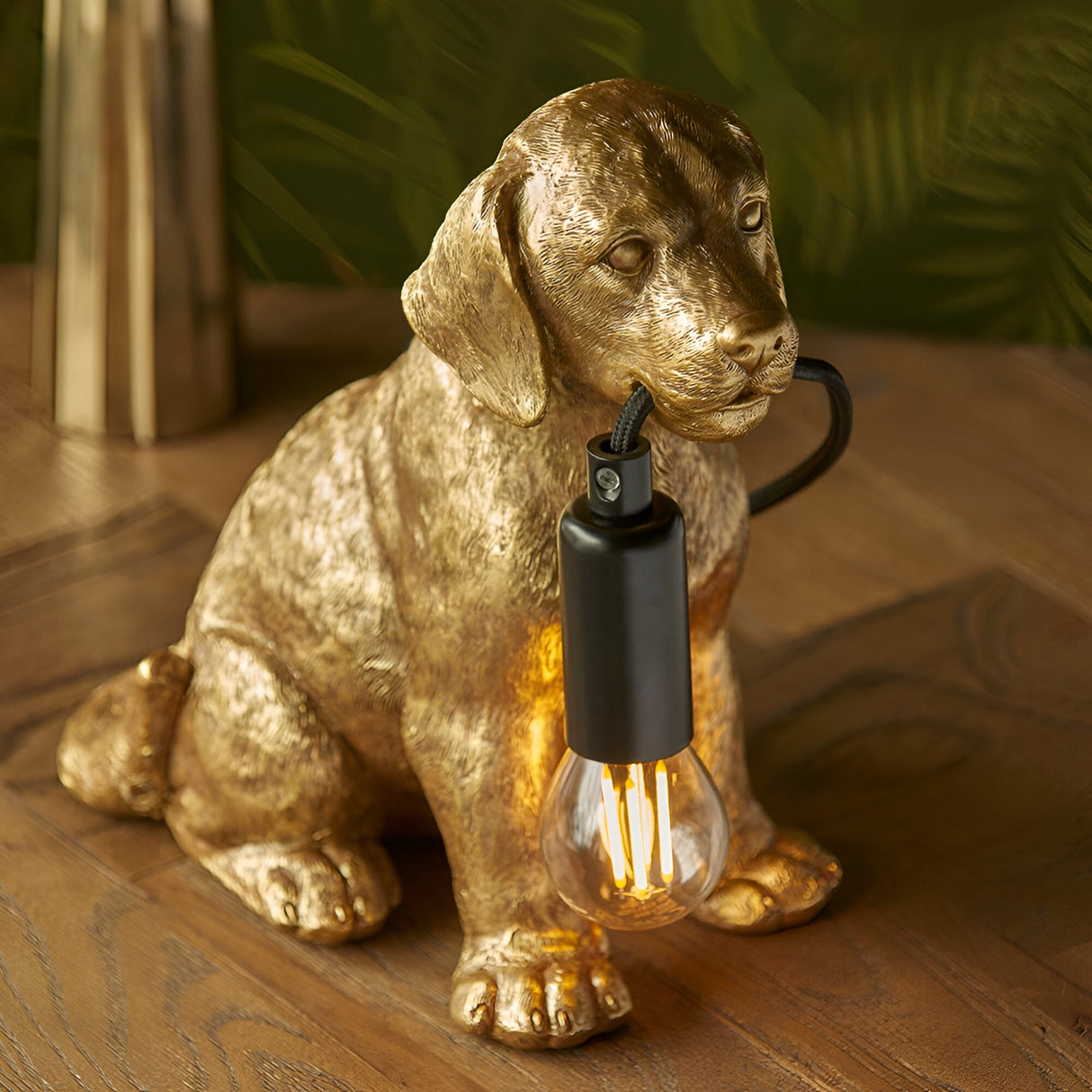 Brockworth Table Lamp resin Labrador puppy figurine in vintage gold, holding a black lamp holder with exposed filament bulb, set on a wooden surface.