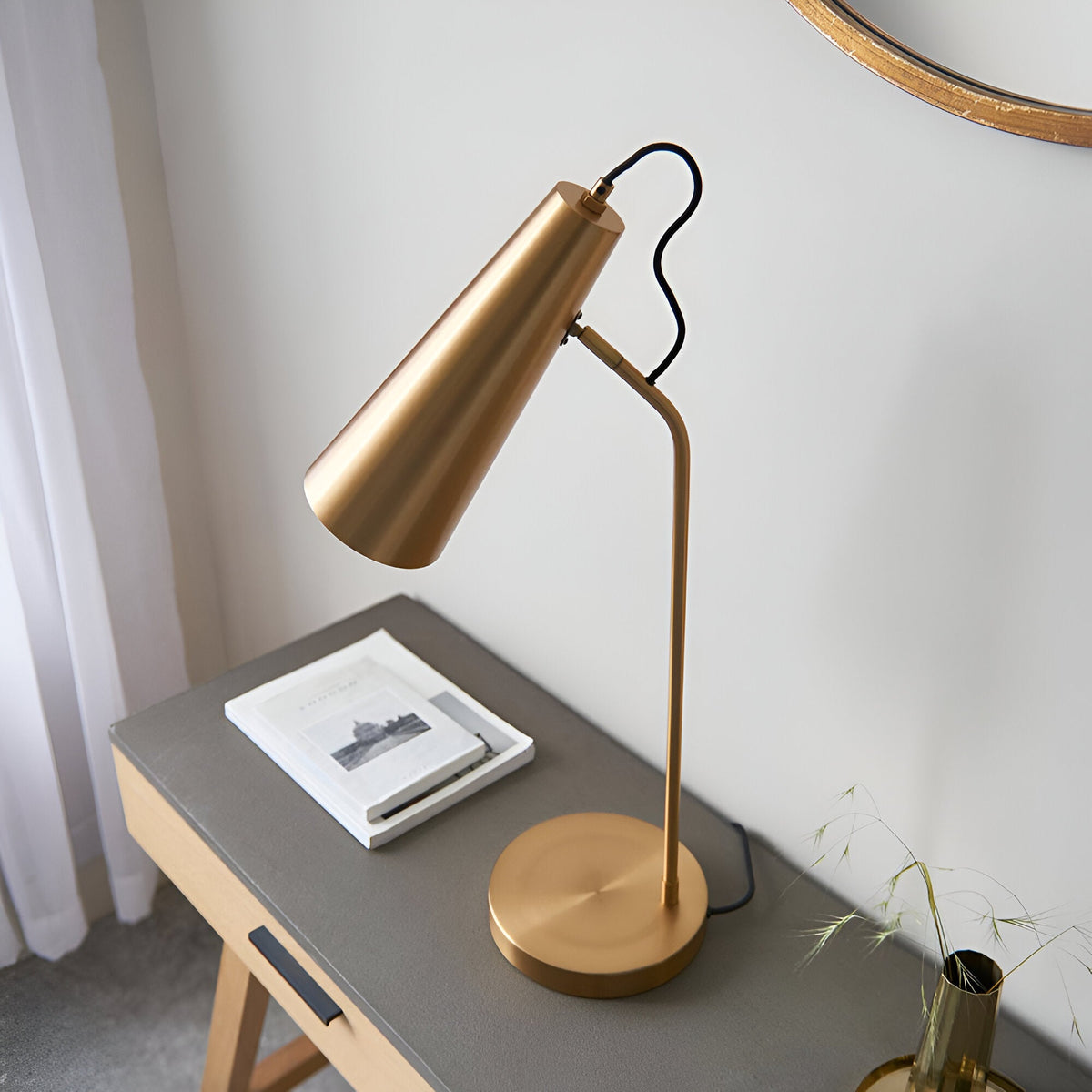 Endon Brockleigh antique brass table lamp with adjustable conical shade and E27 fitting on a grey desk beside a book, styled in a bedroom setting.