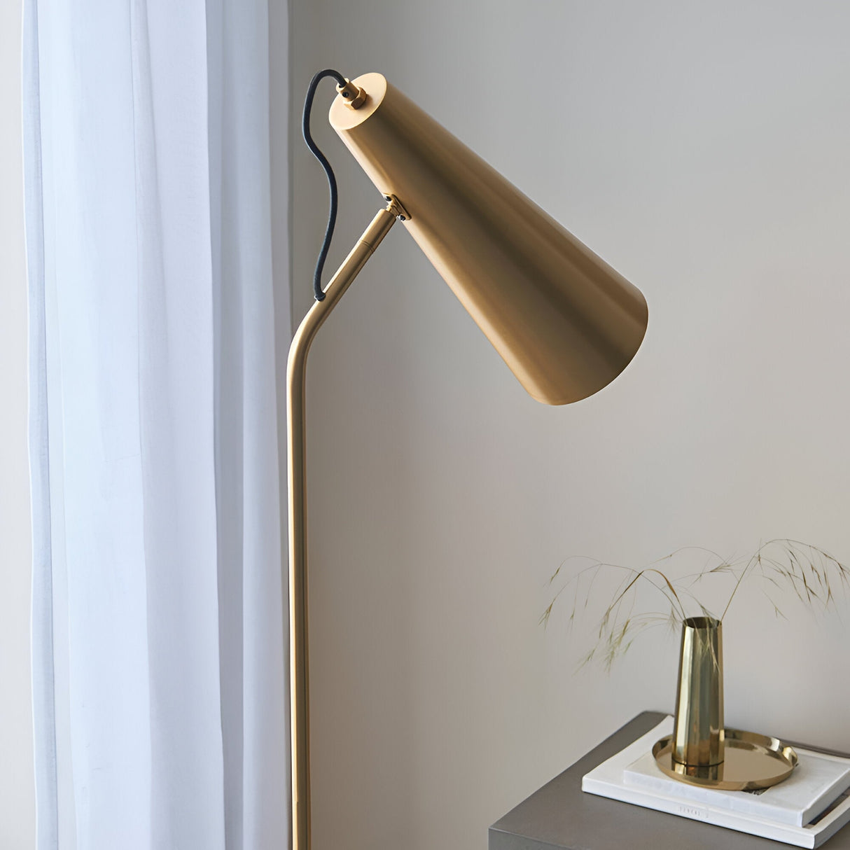 Brockleigh Task Floor Lamp in antique brass, with adjustable cone shade and tall slim pole, shown beside a curtained window and bedside table.