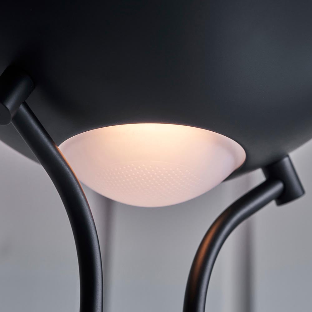 Close-up of the Endon Cliffcombe Floor Lamp in matt black, showing the underside of the uplighter with its opal glass shade glowing warmly between curved arms.