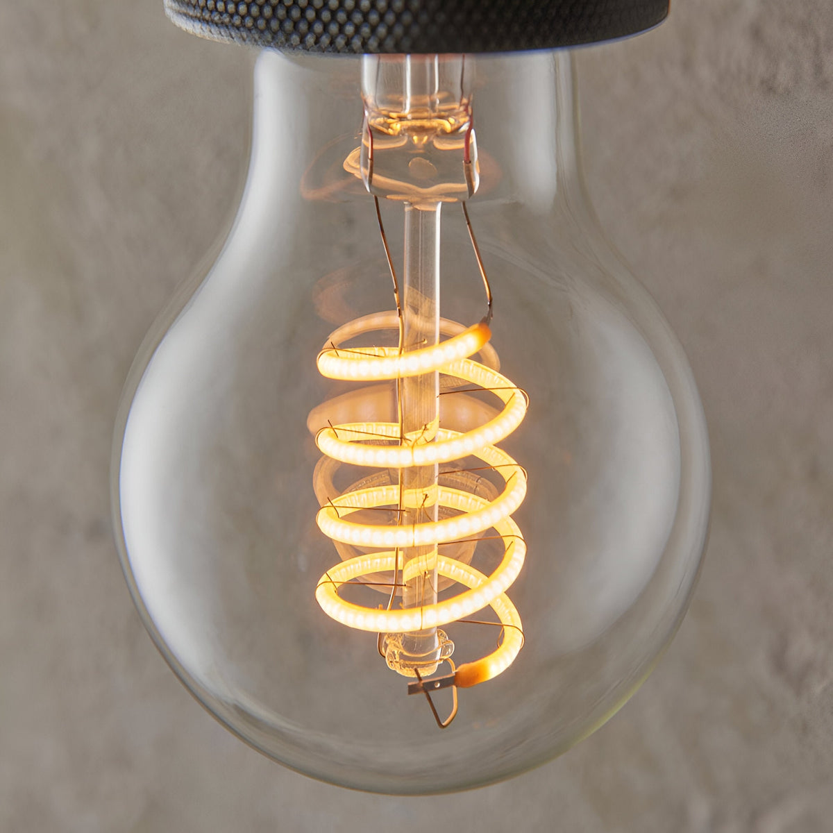 Close-up of a 4W E27 LED filament GLS bulb with clear glass, glowing warm white spiral filament, against a soft neutral background.