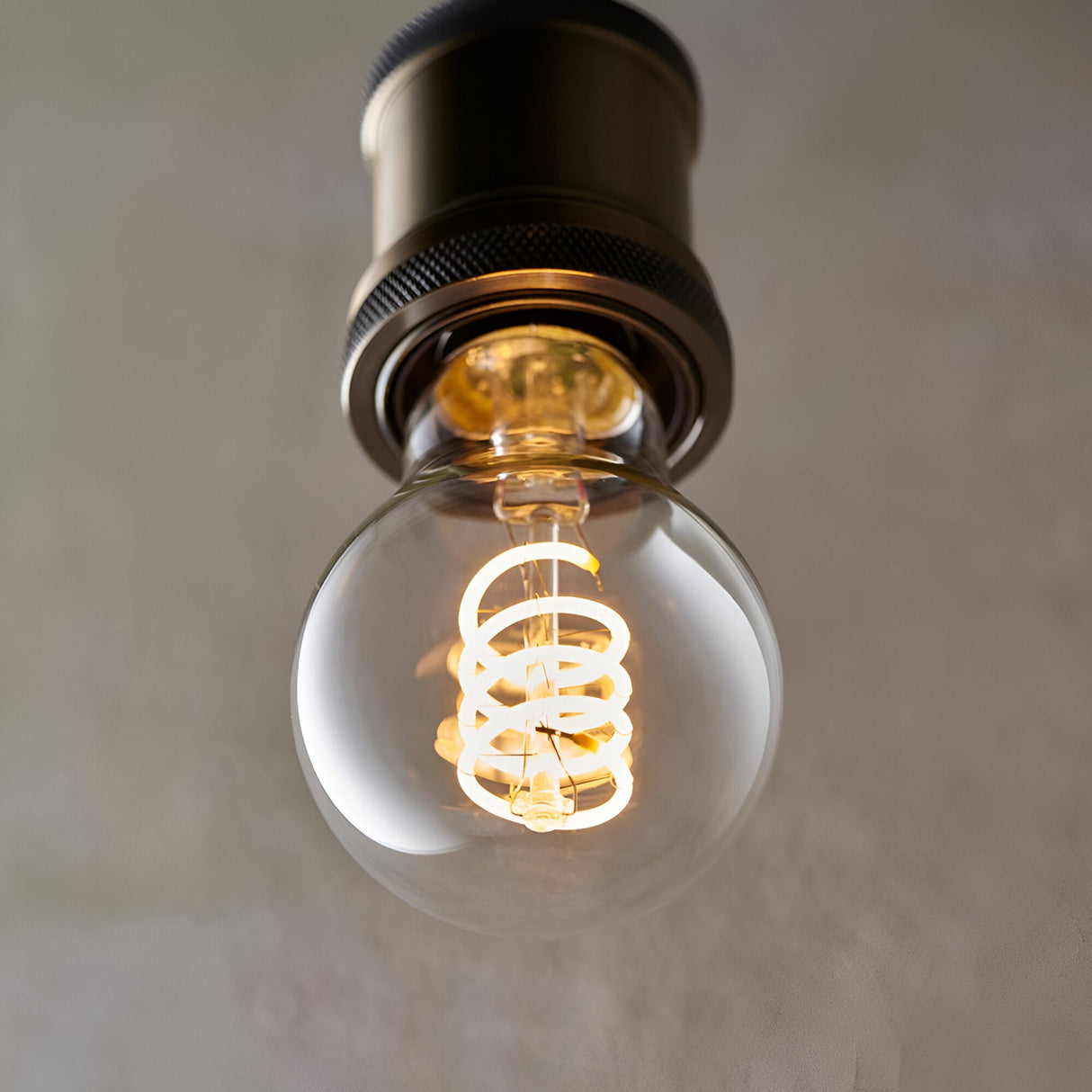 4W E27 LED filament GLS bulb with clear glass and spiral filament, warm white glow, fitted in a dark bronze pendant holder.
