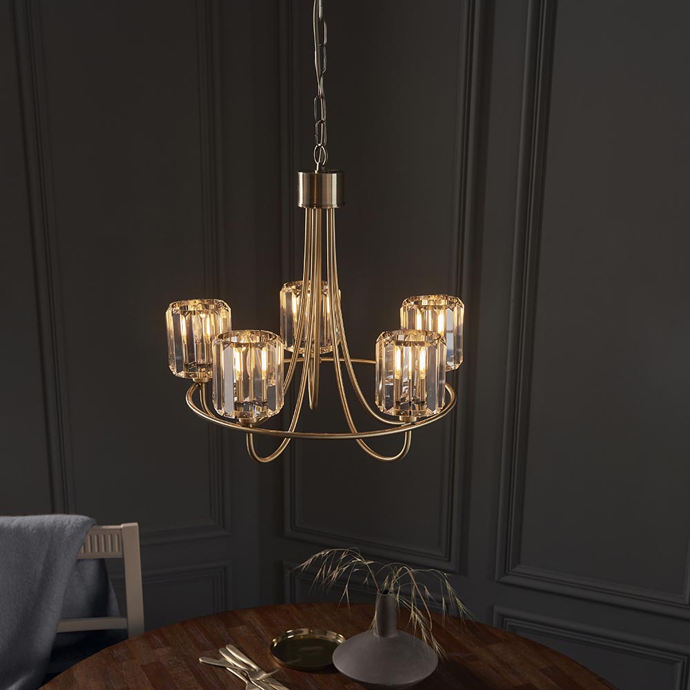 Endon Clementine 5 light brass pendant with cut faceted glass shades on curved arms, hanging from a chain above a wooden dining table.