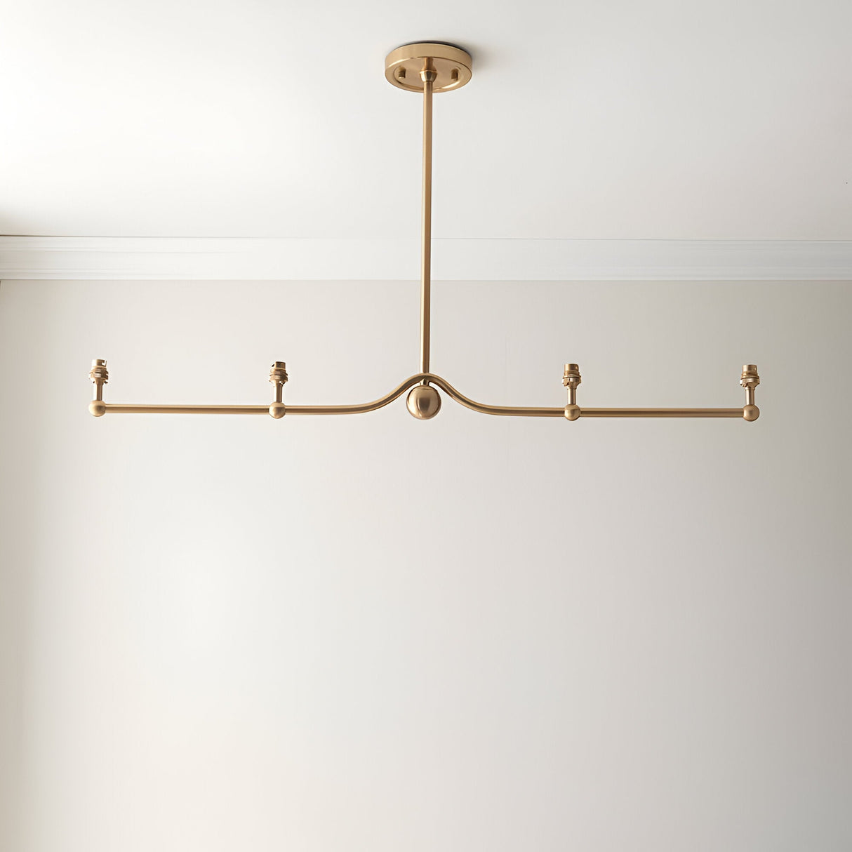 Endon Cliffleigh 4 light linear pendant in brushed aged brass, with a curved bar, sphere detail and B22 lamp holders, shown without shades on a white ceiling.