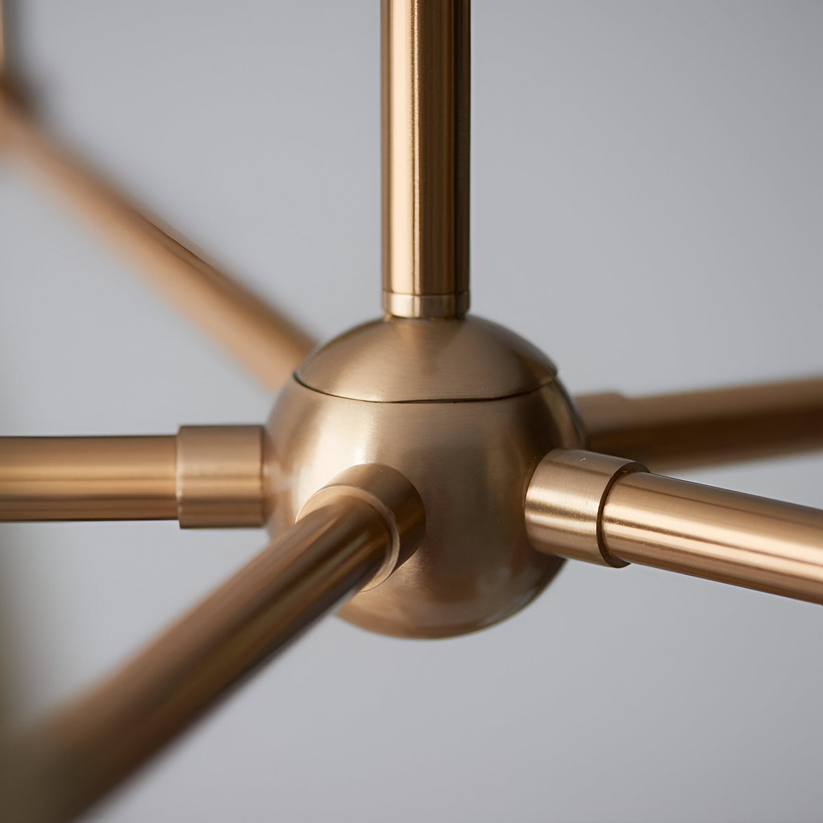 Close-up of the Cliffleigh 5 Light Pendant's central brass hub, showing brushed aged brass arms radiating outward against a plain light grey background.
