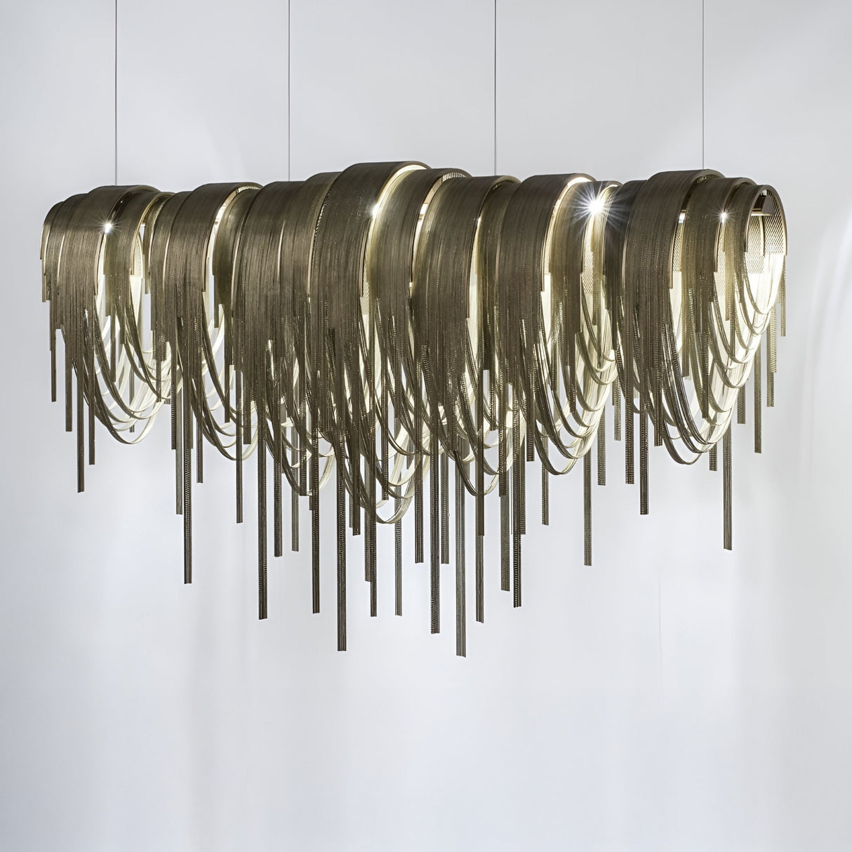 The Symphonia 10 Light Metal Chain Veil Suspension - Gold features cascading brass chains and metallic fringe, creating elegant, wave-like patterns with soft light against a plain white background.