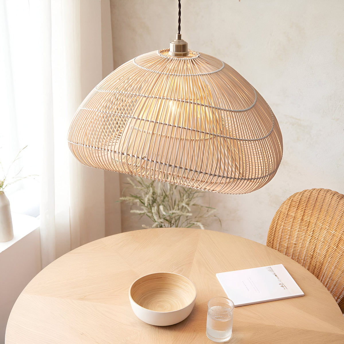 Endon Carlmere natural rattan pendant shade, cloud-shaped hand-woven weave, hung above a round wooden dining table with bowl, glass and wicker chair.