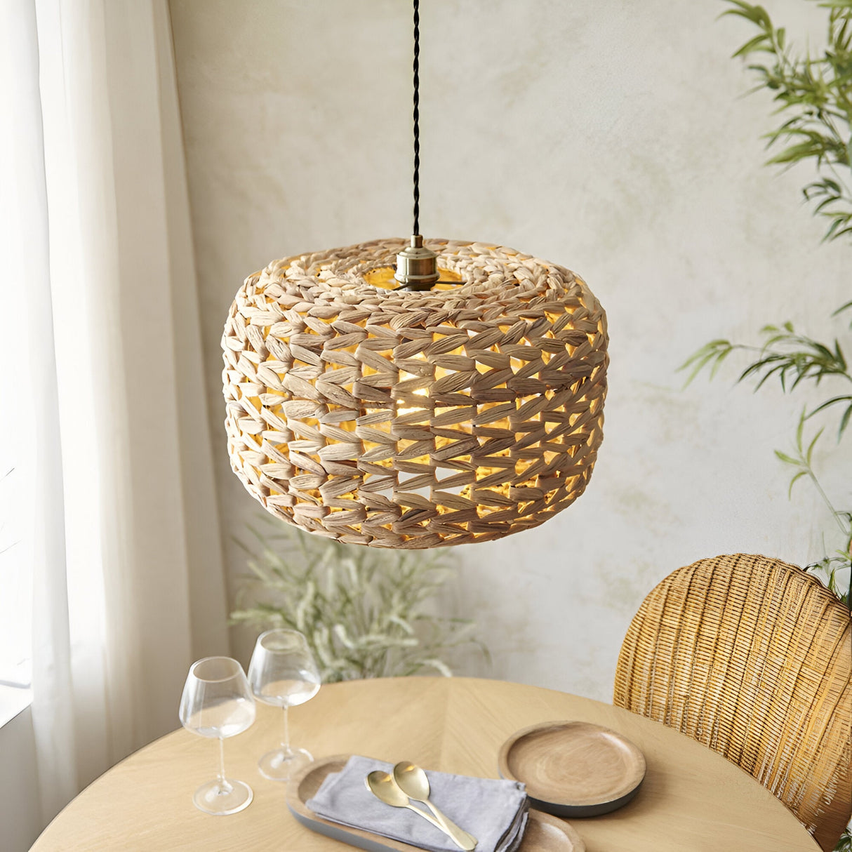 Endon Cranley pendant shade in natural handwoven rattan with a soft rounded open weave, hung above a wooden dining table beside a rattan chair.
