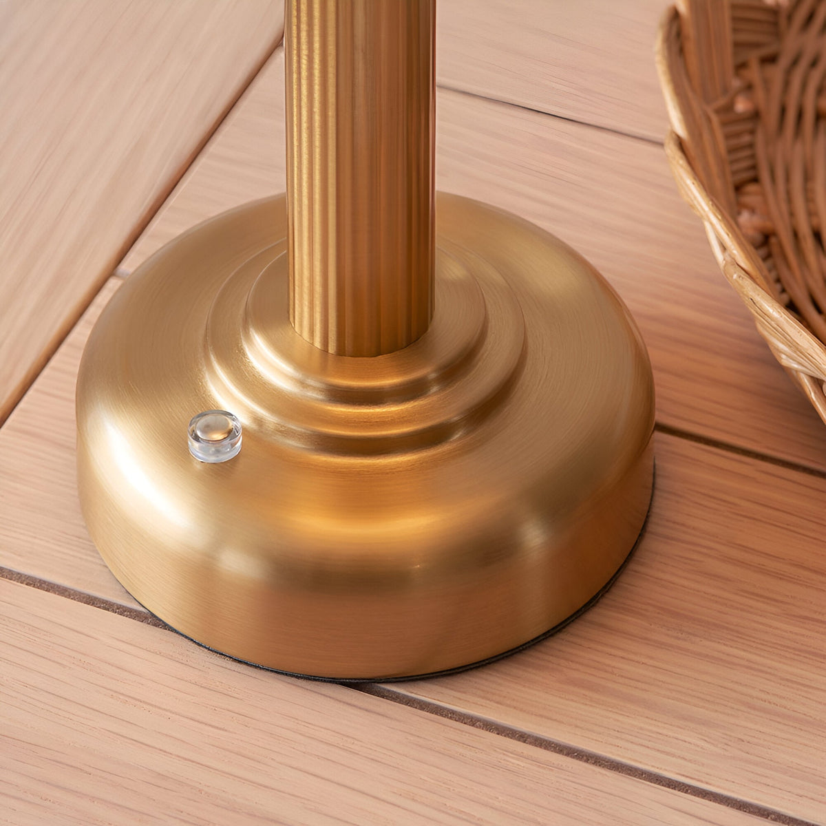 Close-up of the brushed brass fluted stem and rounded base of the Endon Ashfield LED table lamp on light wooden decking beside a wicker basket.