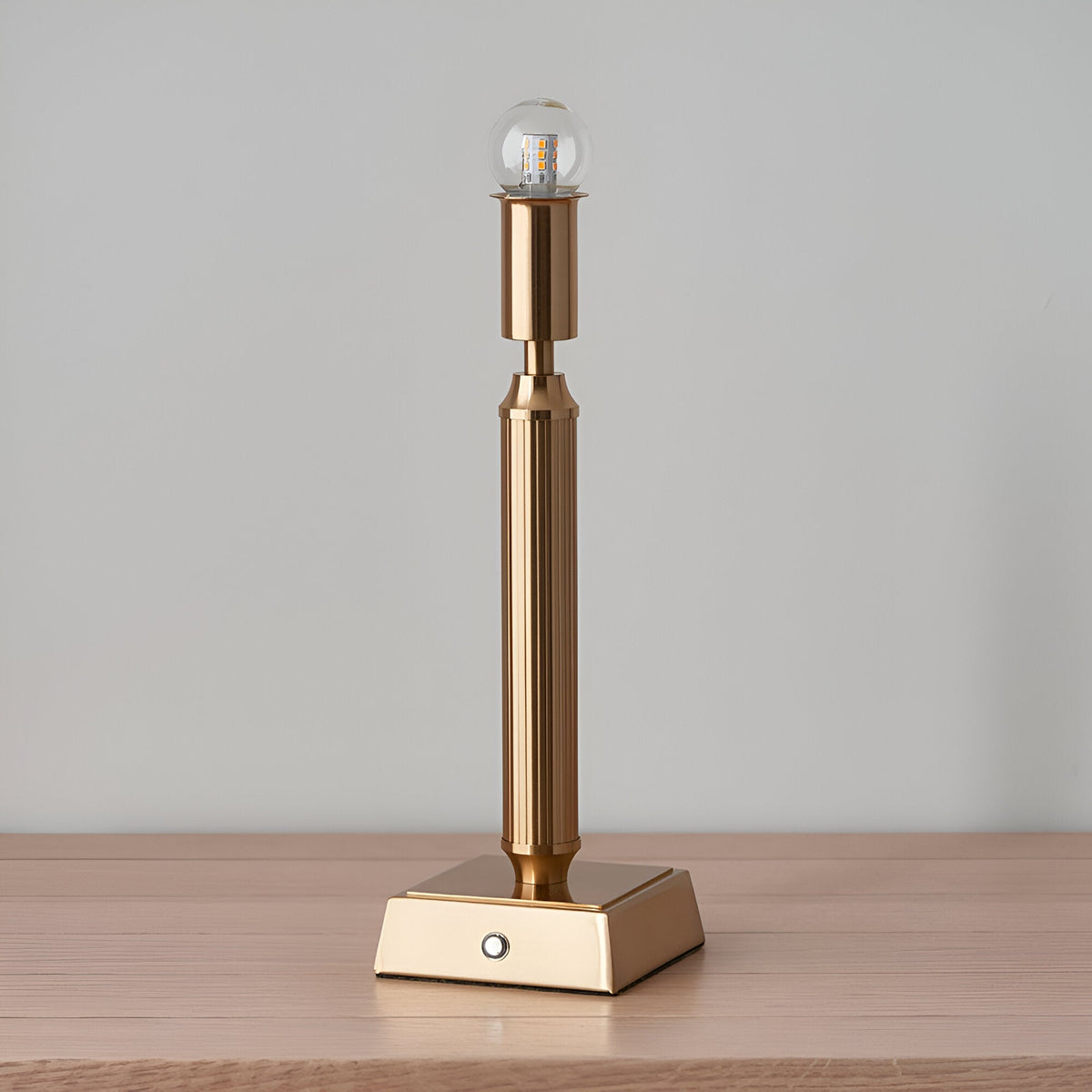 Endon Cranwick LED table lamp in brushed aged brass with reeded stem, square base, touch dimmer button, and clear globe bulb on a wooden surface.