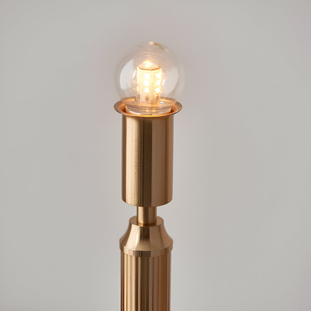 Close-up of the Endon Cranwick LED table lamp's brushed brass stem with lit integrated LED globe bulb, shown against a plain light background.
