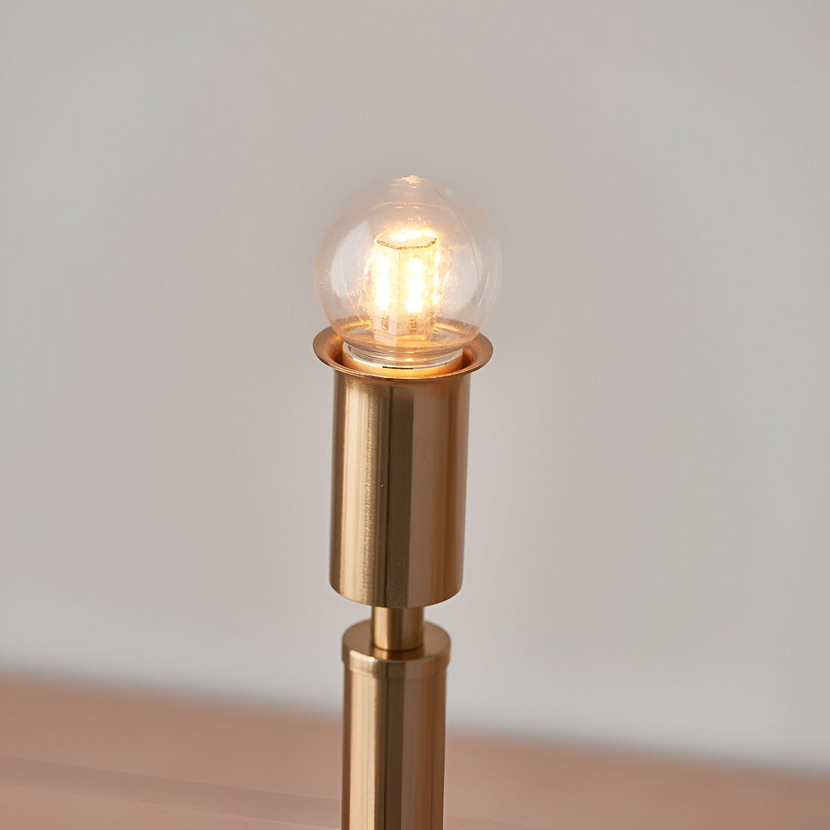 Danebourne LED Table Lamp in brushed aged brass, showing stepped metal base with glowing globe bulb against a plain light background.