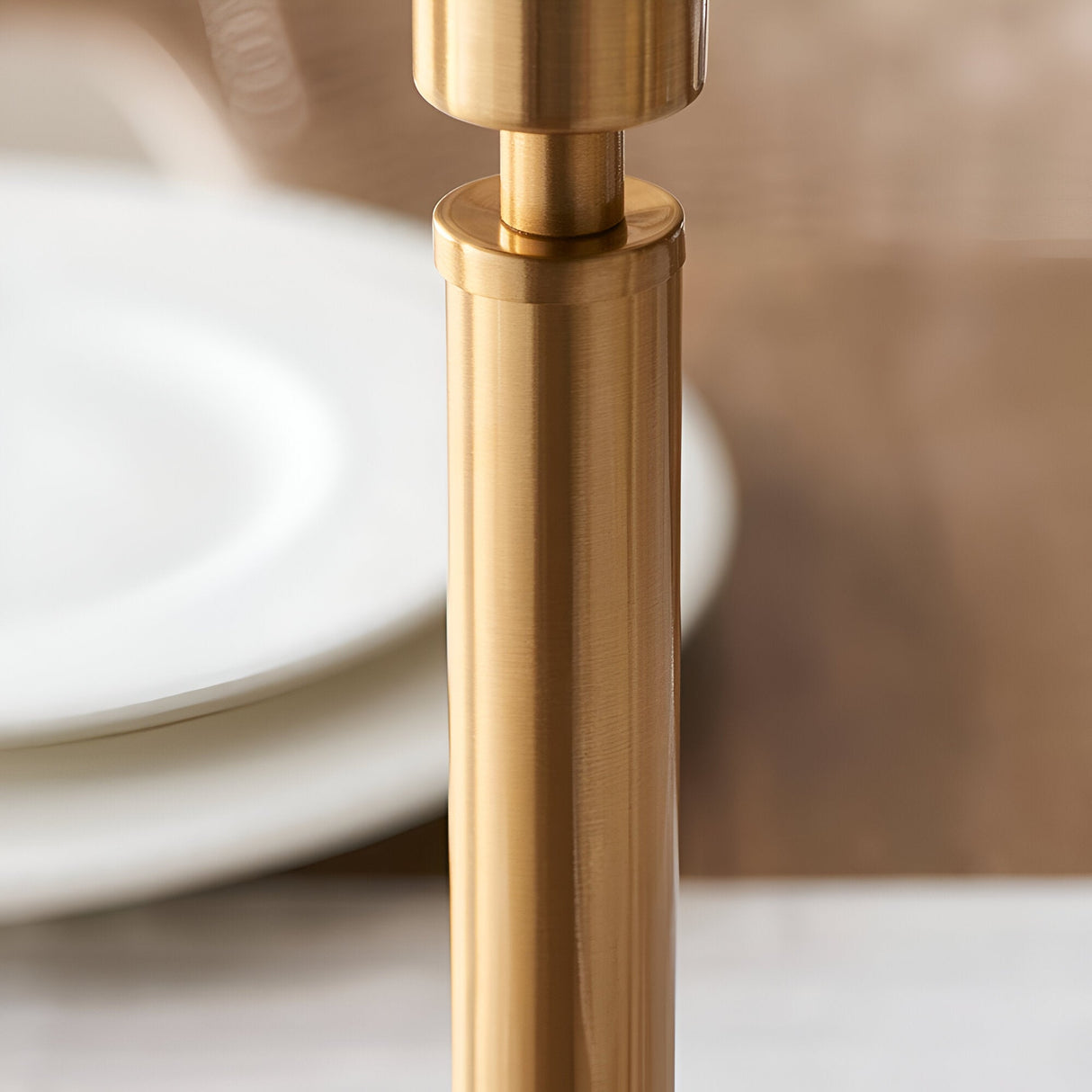 Close-up of the Danebourne LED Table Lamp's brushed aged brass stepped column and touch dimmer, shown beside white plates on a marble surface.