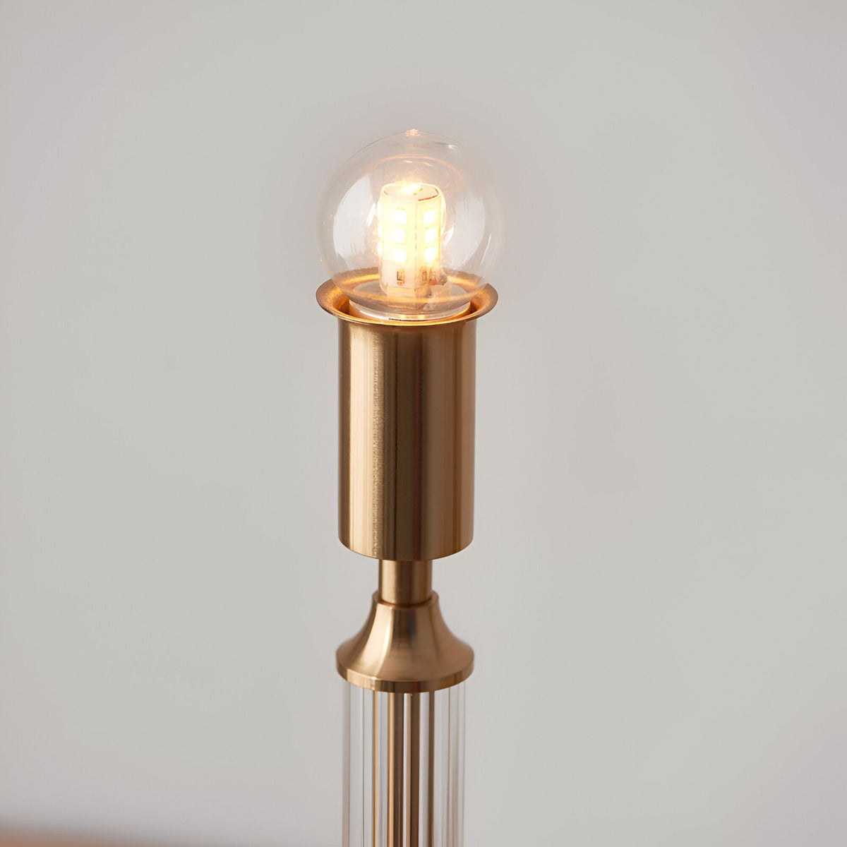 Close-up of the Endon Carlwood LED table lamp's brushed aged brass head with a lit clear globe bulb, shown against a plain light background.