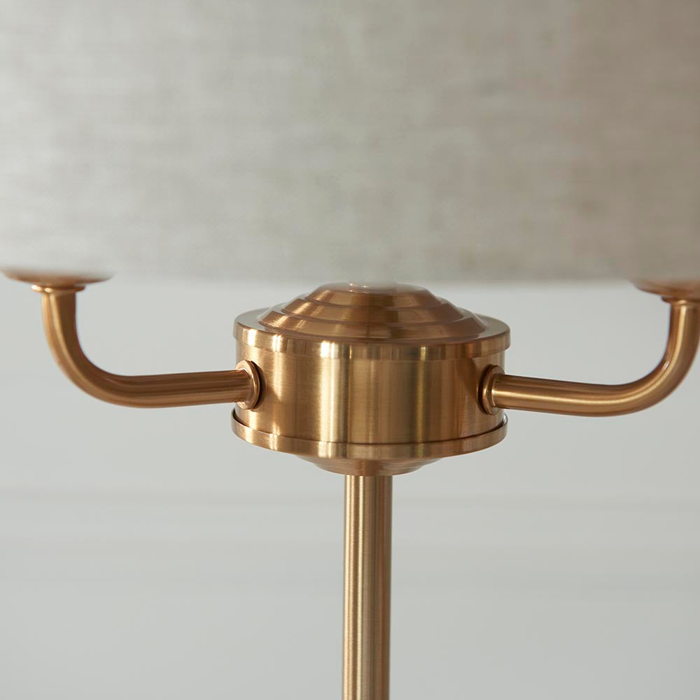 Close-up of the Brenley 3 Light Table Lamp in brass, showing three curved arms meeting a ribbed brass column beneath a linen shade.