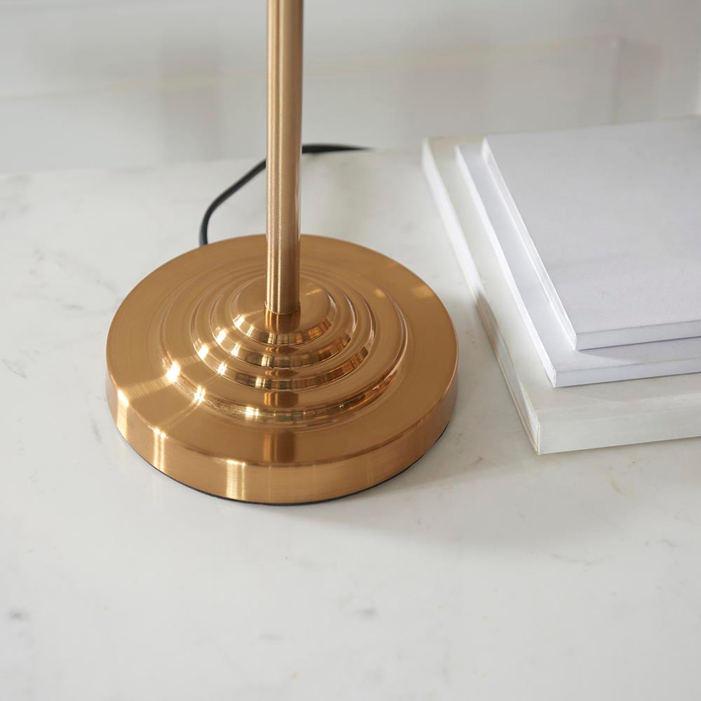 Brenley 3 Light Table Lamp base close-up in brushed brass with ribbed stepped design, shown beside white notepads on a marble surface.