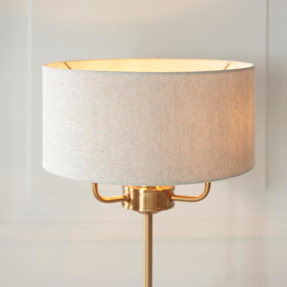 Brenley 3 Light Table Lamp in brass, with a round linen-mix drum shade and brushed metallic inner lining atop a slender brass base.