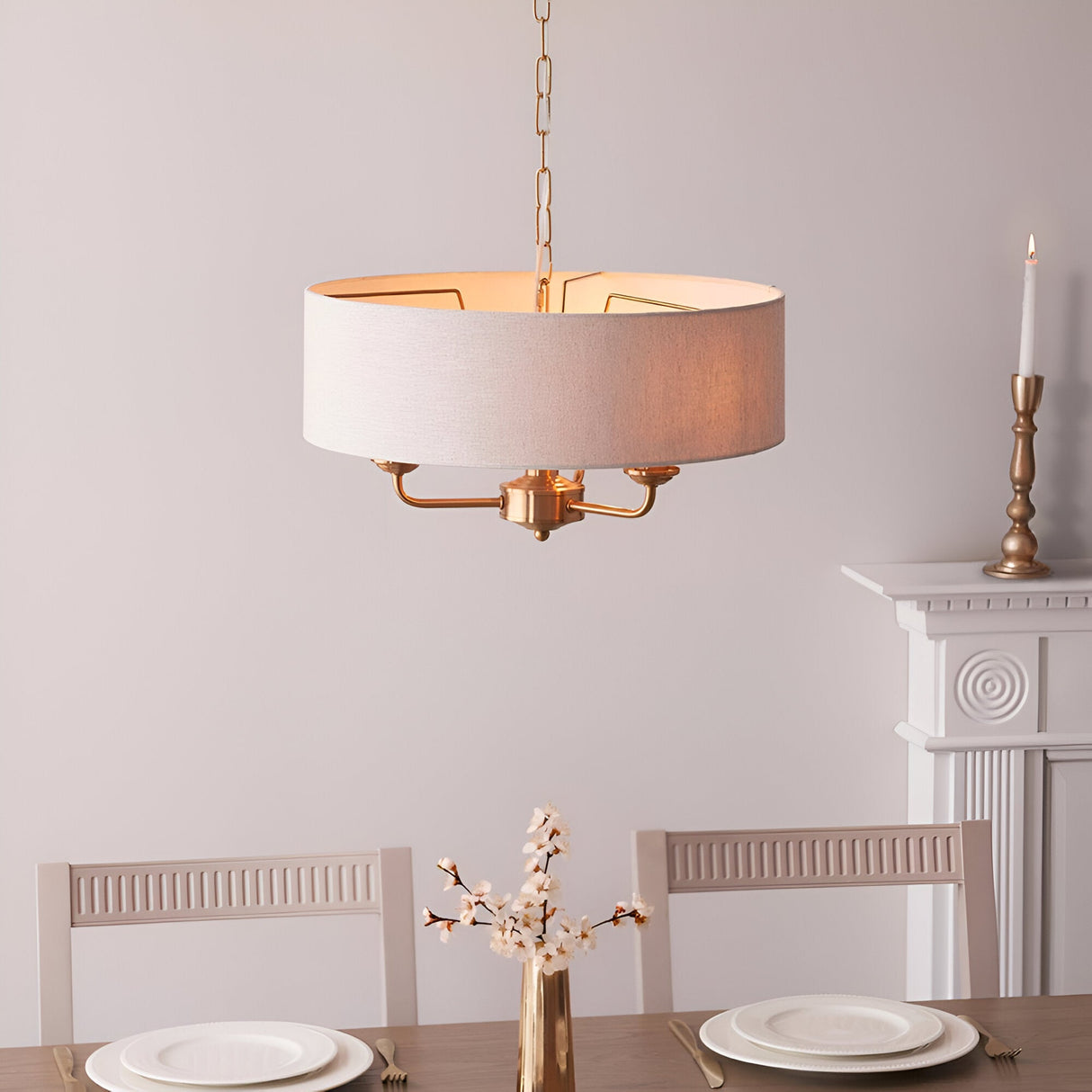Brenley 3 Light Pendant in vintage brass with a natural linen drum shade, hung on chain above a dining table in a light-toned room.