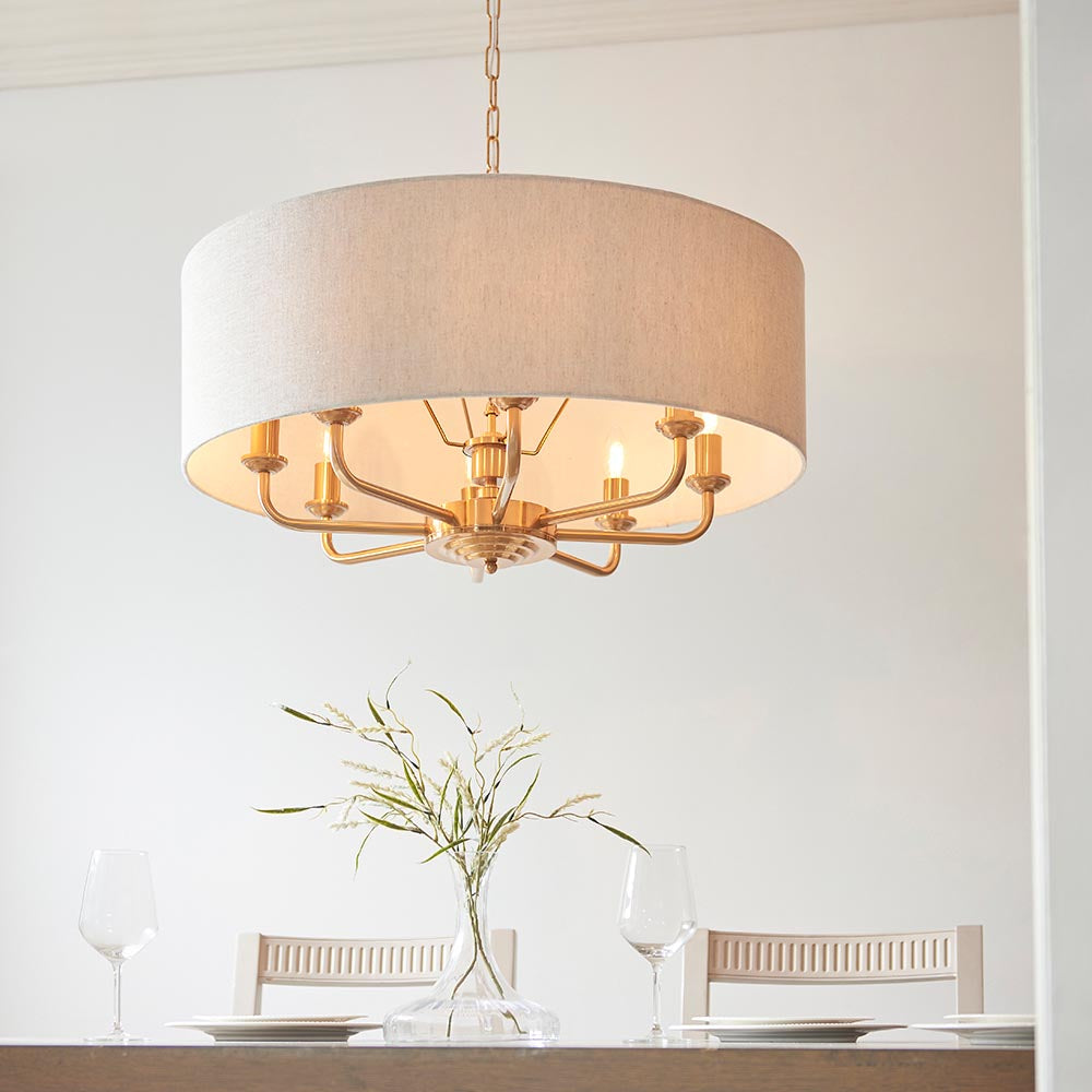 Endon Brenley 8 light pendant in vintage brass with a large natural linen drum shade, hanging above a dining table in a bright room.
