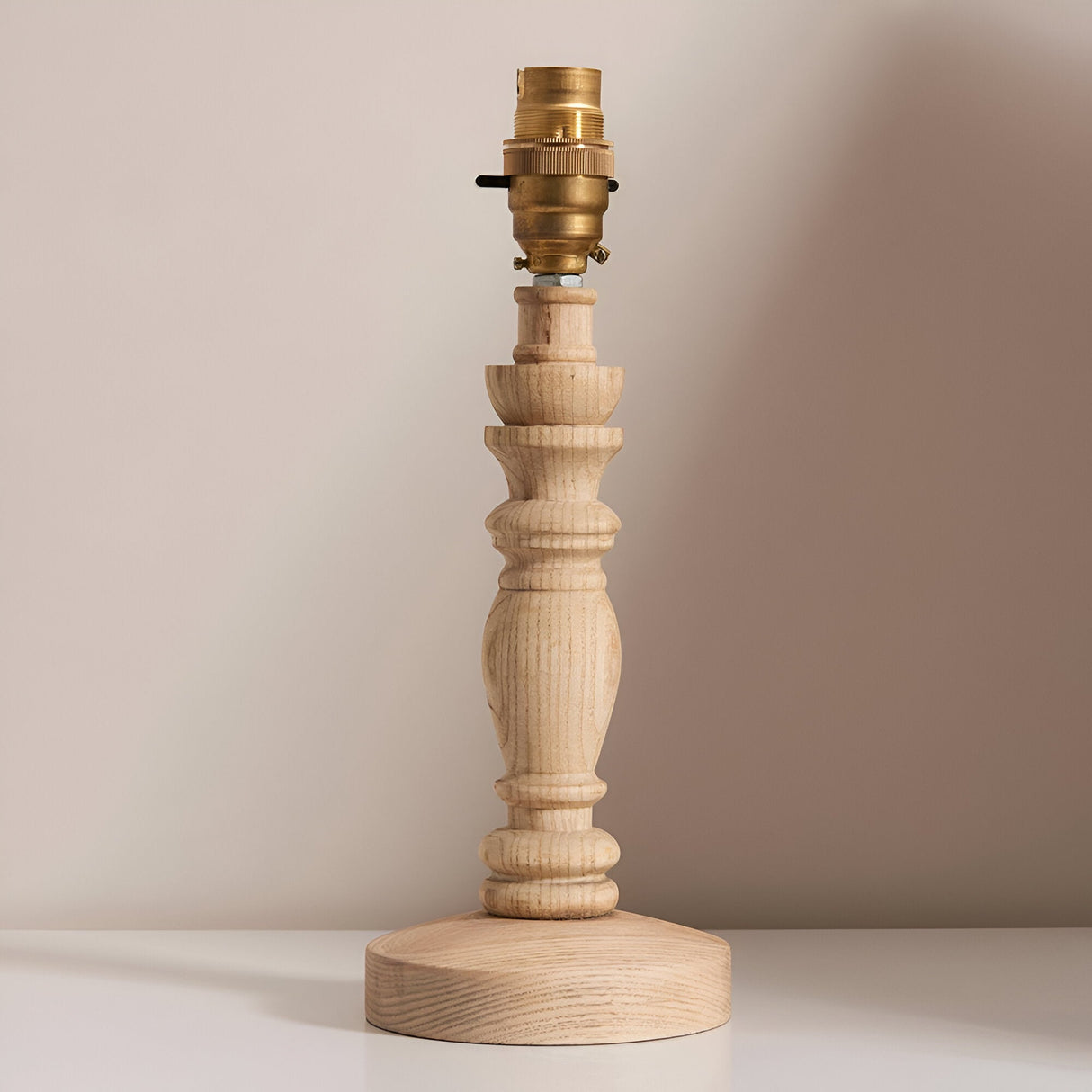 Endon Aldworth table lamp with turned natural ash wood spindle base and brass B22 switched lampholder, shown without shade on a light neutral background.
