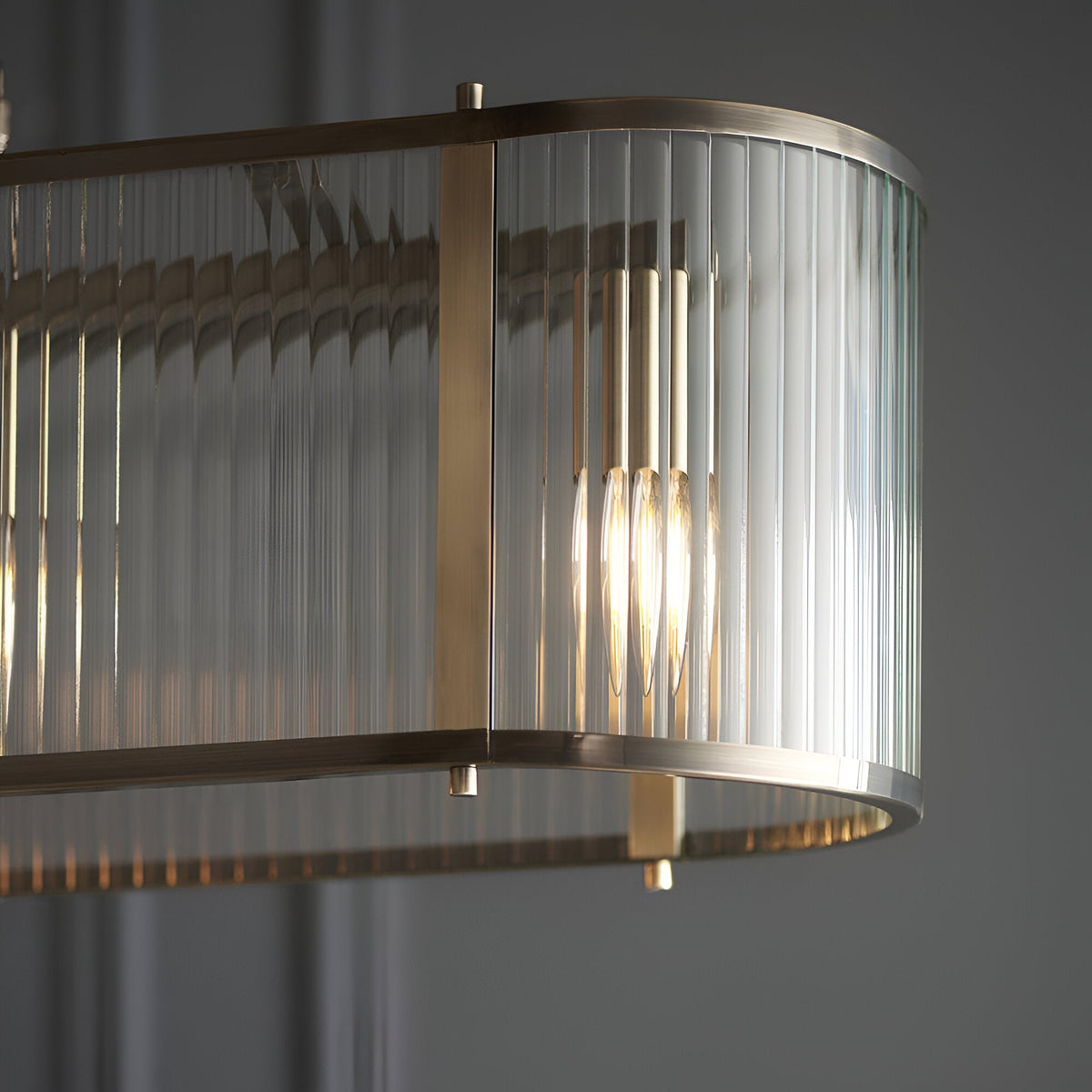 Rothbury 4 Light Linear Pendant close-up showing ribbed glass panels and antique brass frame with lit E14 bulbs inside.