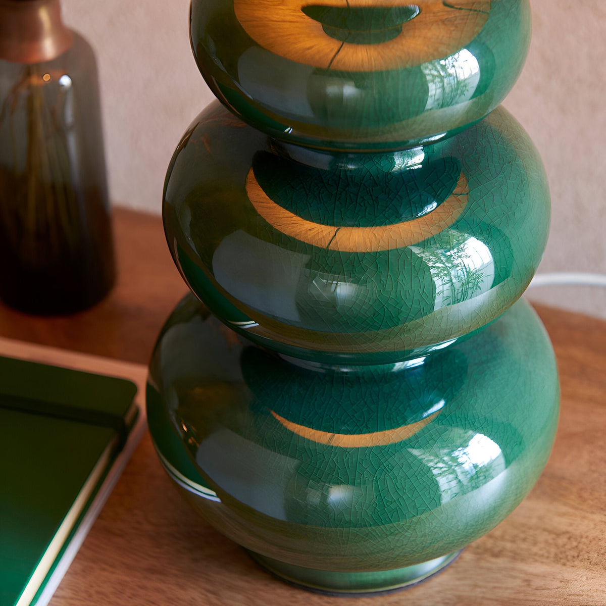 Endon Carlstead table lamp base in gloss green reactive glaze ceramic with stacked gourd curves, styled on a wooden surface beside a green notebook.