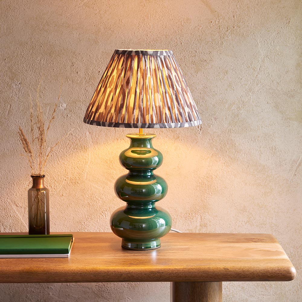 Endon Carlstead gourd-shaped green ceramic table lamp with brass fitting and patterned pleated shade, on a wooden console beside a dried grass vase.