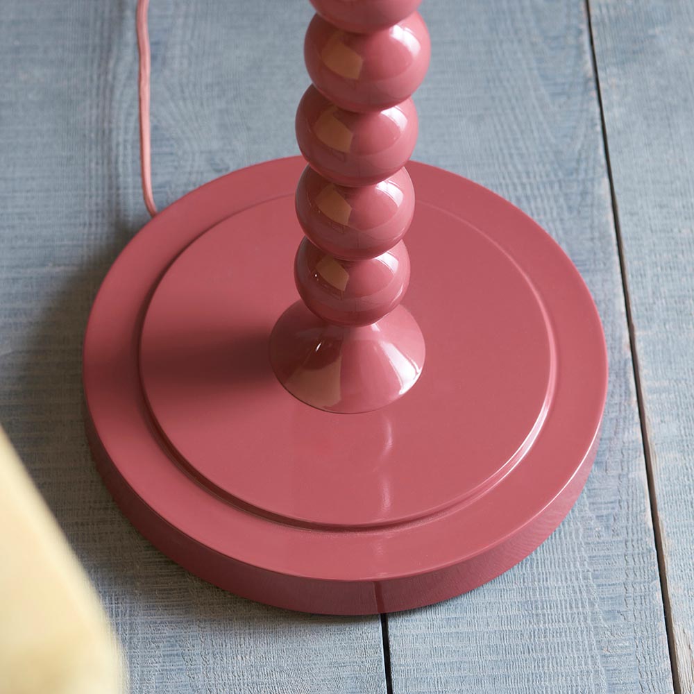 Close-up of the Endon Brenleigh floor lamp base in glossy pink clay, showing stacked metal spheres on a round base against blue-grey plank flooring.