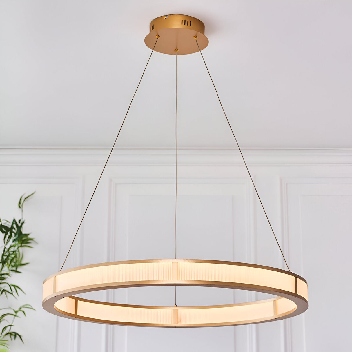Endon Bevley large LED ring pendant in brushed gold with ribbed frosted acrylic diffuser, suspended on clear cables against a white panelled wall.