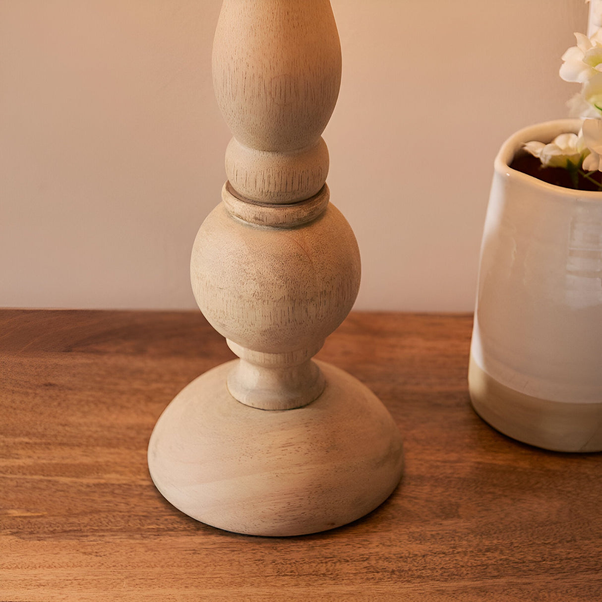 Close-up of the Endon Brenhurst table lamp base, hand-turned solid natural wood with turned ball and bulb shapes, shown on a wooden surface beside a cream vase.
